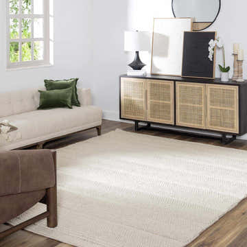 Living room scene with cream Alora Area Rug, sofa with green pillows, and a rattan cabinet. Roomscene-Rectangle