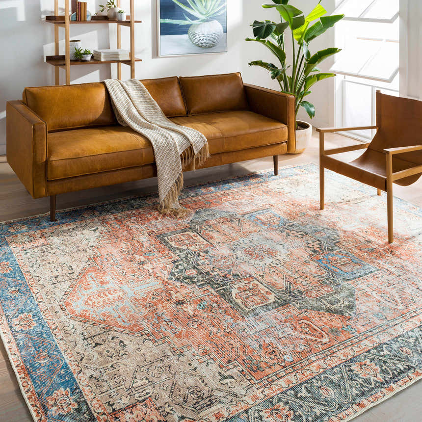 Living room scene with a Livabliss Amelie AML-2309 rug, tan sofa, wood chair, and bookshelf. The rug has beige, rust, and blue tones. Roomscene-Rectangle