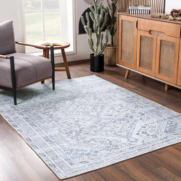 Living room scene with Barny Gray Denim Washable Rug, gray armchair, wood cabinet, cactus, and natural light. Roomscene-Rectangle