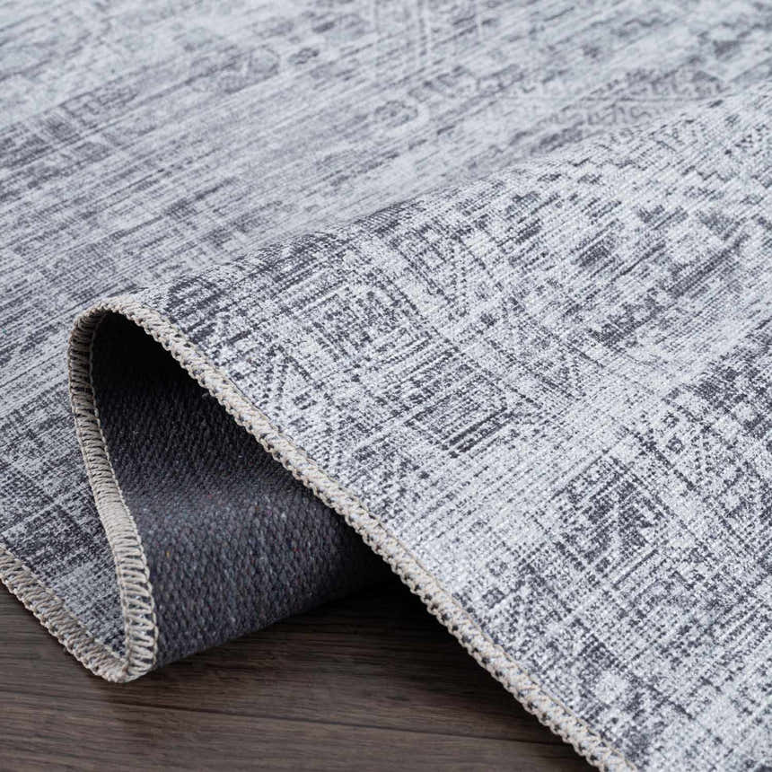 Close up of the Barny Gray Blue Washable Rug showing its chenille texture, gray and off-white colors, and woven backing. Fold