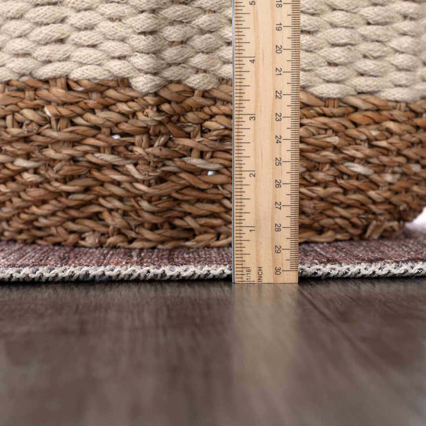Close up of Barny Brown Flat Pile Washable Rug showing its texture, thin profile, and edge binding next to a ruler. Pile