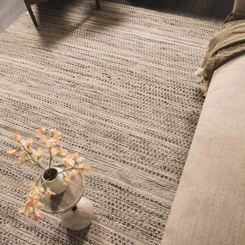 Close up of the hand woven Arabi Wool Area Rug in a living room setting. The rug is black, gray, and light beige. Styleshot