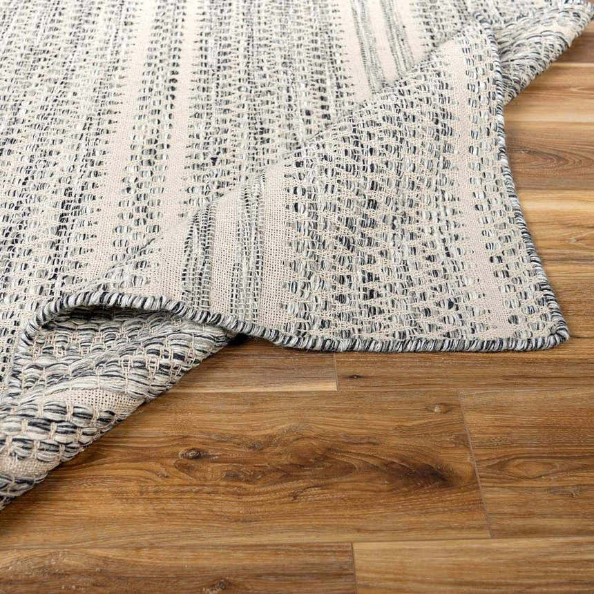 Close-up of the hand-woven Arabi Wool Area Rug showing its black, gray, and light beige textured design. Fold