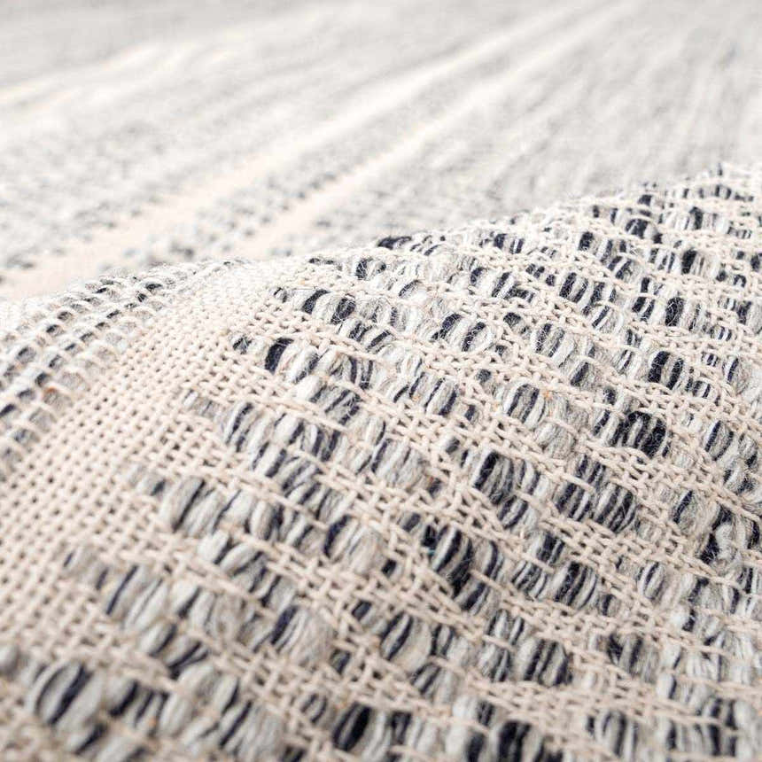Close-up of the hand-woven Arabi Wool Area Rug, showing its black, gray, and light beige pattern and texture. Fold