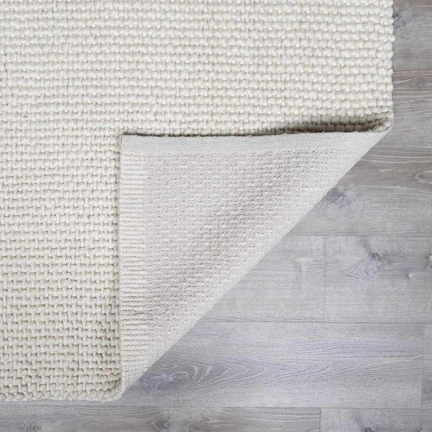 Close-up of the textured, hand-woven Lucerne Plain Cream Wool Rug LNE-1000 showing the backing. Fold