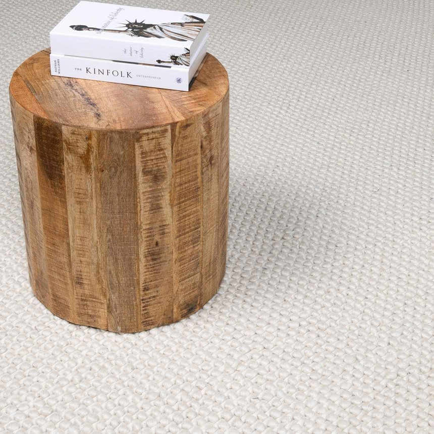 Close-up of the cream Lucerne Plain Wool Rug, with a textured weave and a rustic wood side table. Styleshot