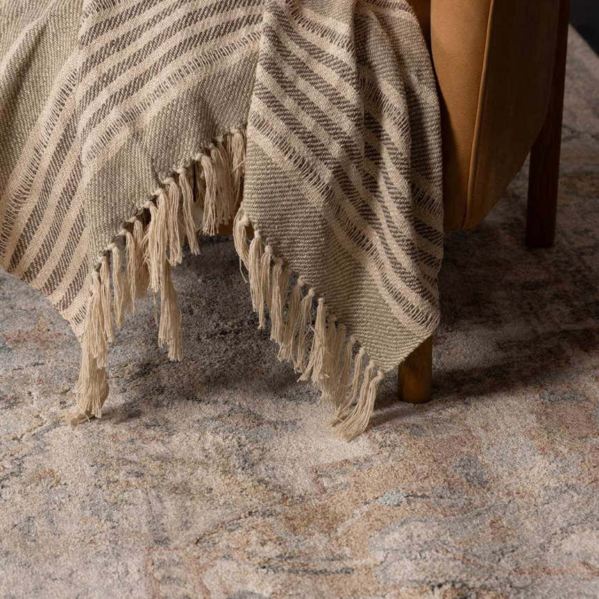 Close-up of the Vaeda Blue & Beige Thick Luxe Rug with beige, tan, and blue tones under a chair with a fringed throw. Styleshot
