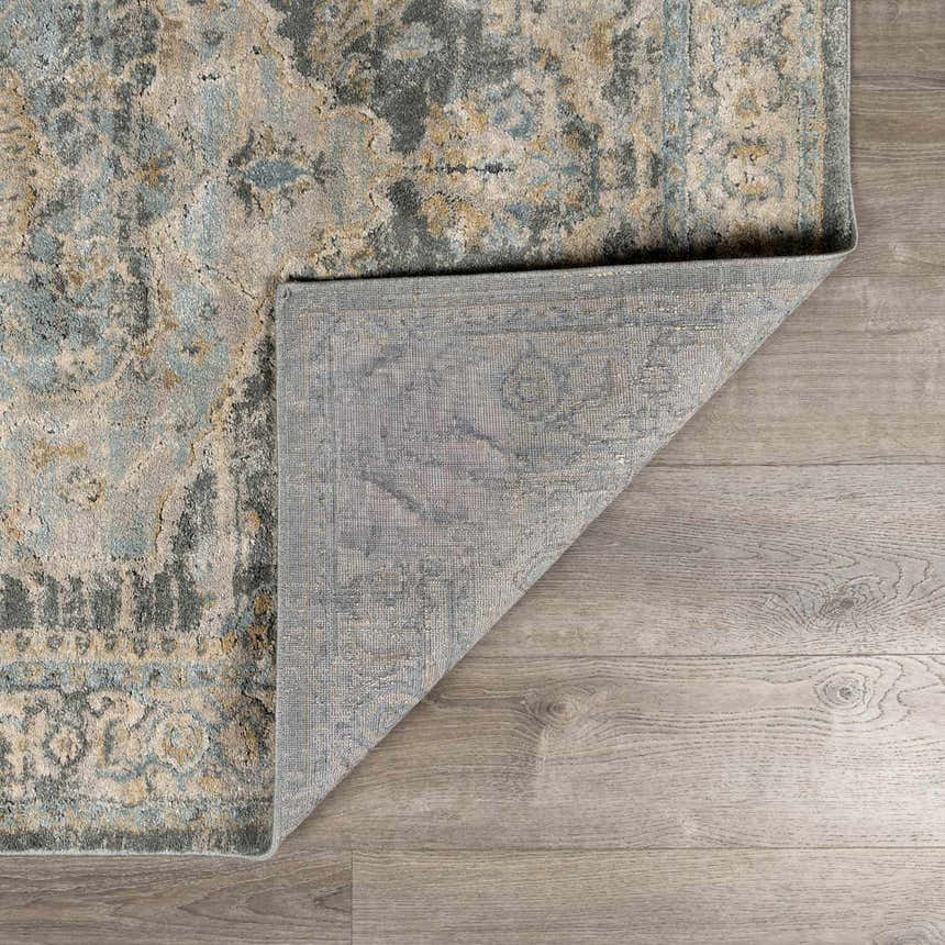Close-up of the Vaeda Blue Thick Luxe Rug showing its beige, gray, and blue traditional pattern and machine-woven construction. Fold