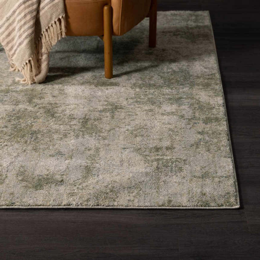 Close-up of the Zazie Thick Luxe Rug in olive and beige, styled with a leather chair and blanket on dark wood floors. Styleshot