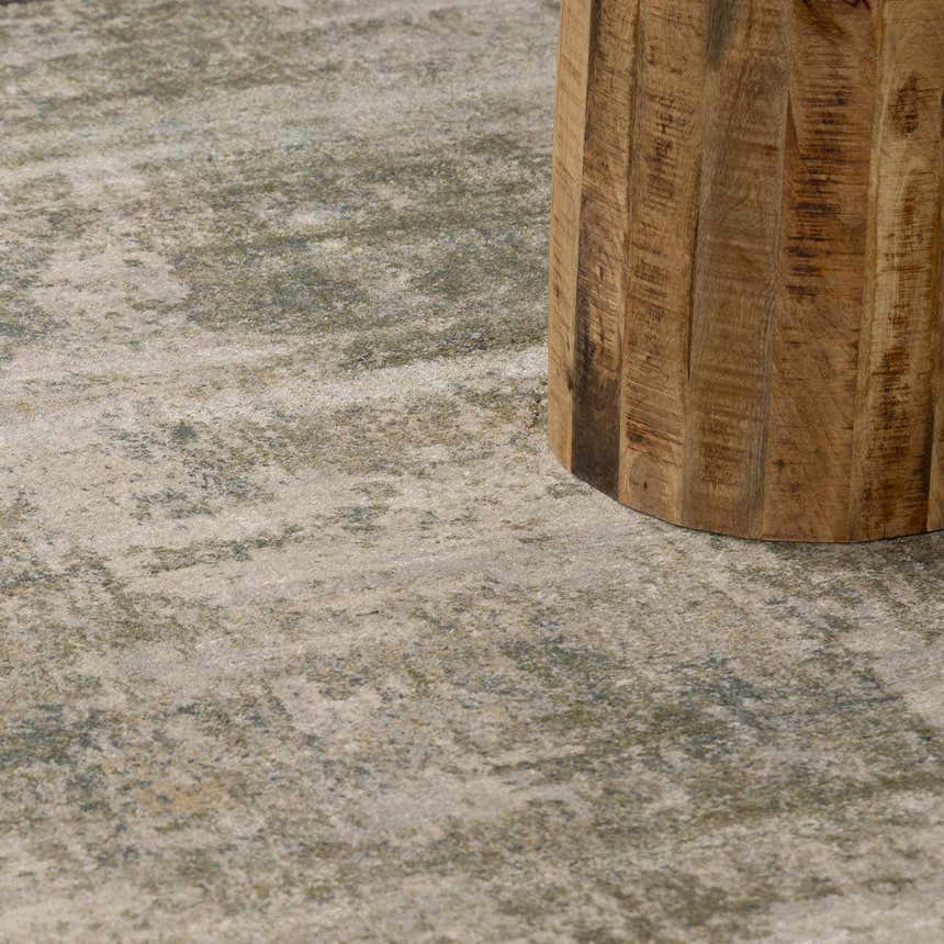 Close-up of the beige and gray Zazie Thick Luxe Rug with an abstract pattern and a textured wood table leg. Styleshot