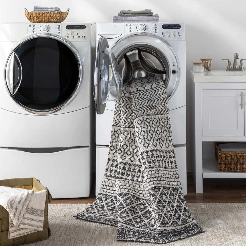 Laundry room scene with Barnwood Washable Area Rug emerging from the washing machine. Bohemian black and cream geometric pattern. Washing-Machine