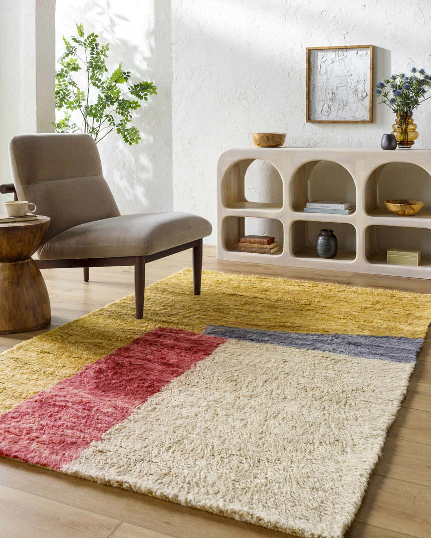 Living room scene with a Budrys Wool Area Rug in brick red, camel, tan and pearl, styled with a modern chair and light wood console table. Roomscene-Rectangle