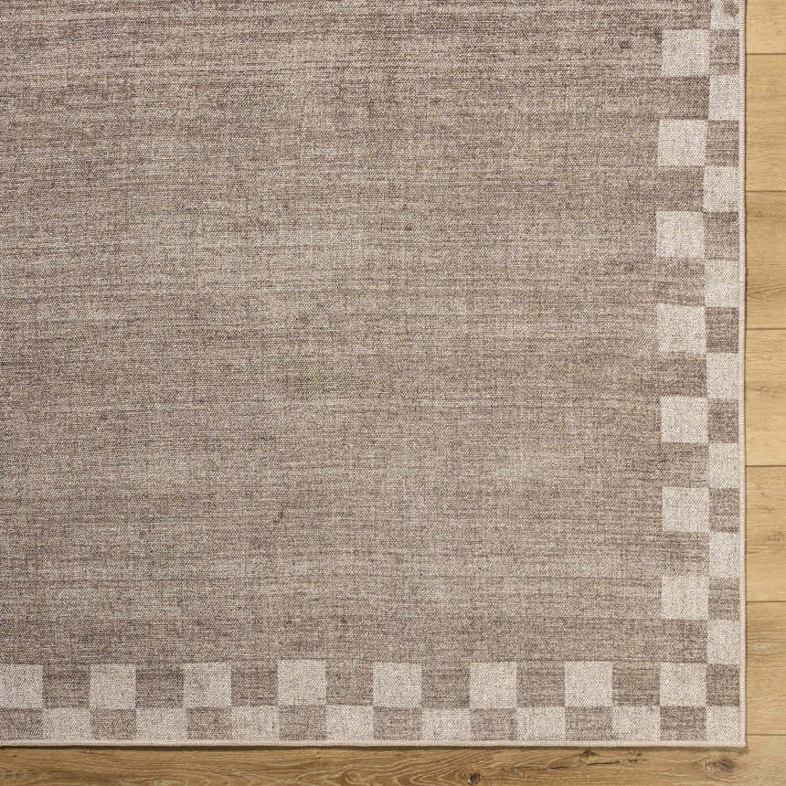 Close up of the Bardot Washable Area Rug showing a neutral color and a checkerboard border on a wood floor. Corner
