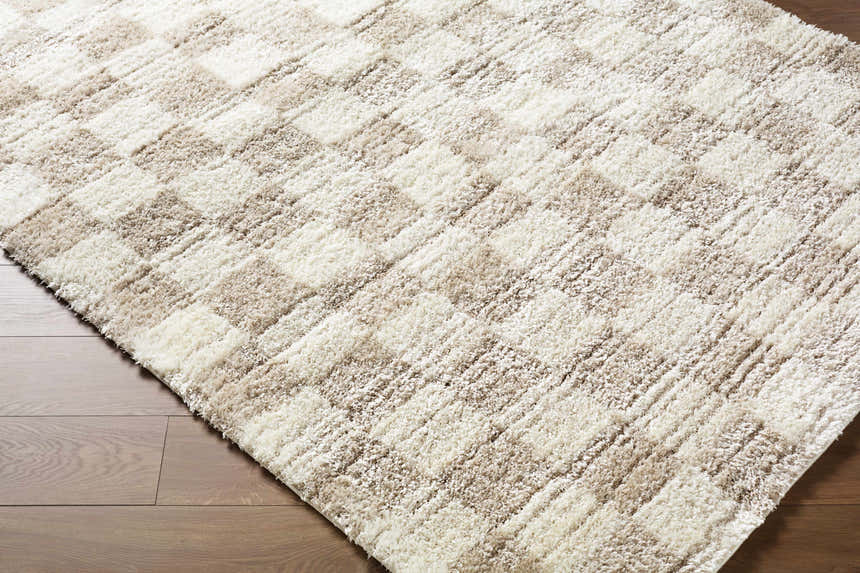Close-up of the Belita Beige Luxe Shag Area Rug showing its cream and tan checkered pattern and plush, soft texture. Corner