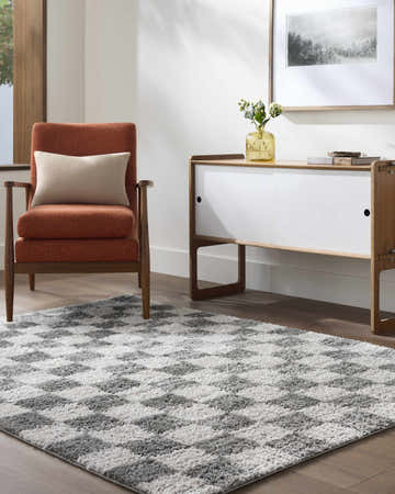 Living room scene with an orange chair and the Belita Charcoal Luxe Shag Area Rug in a gray and white geometric pattern. Roomscene-Rectangle