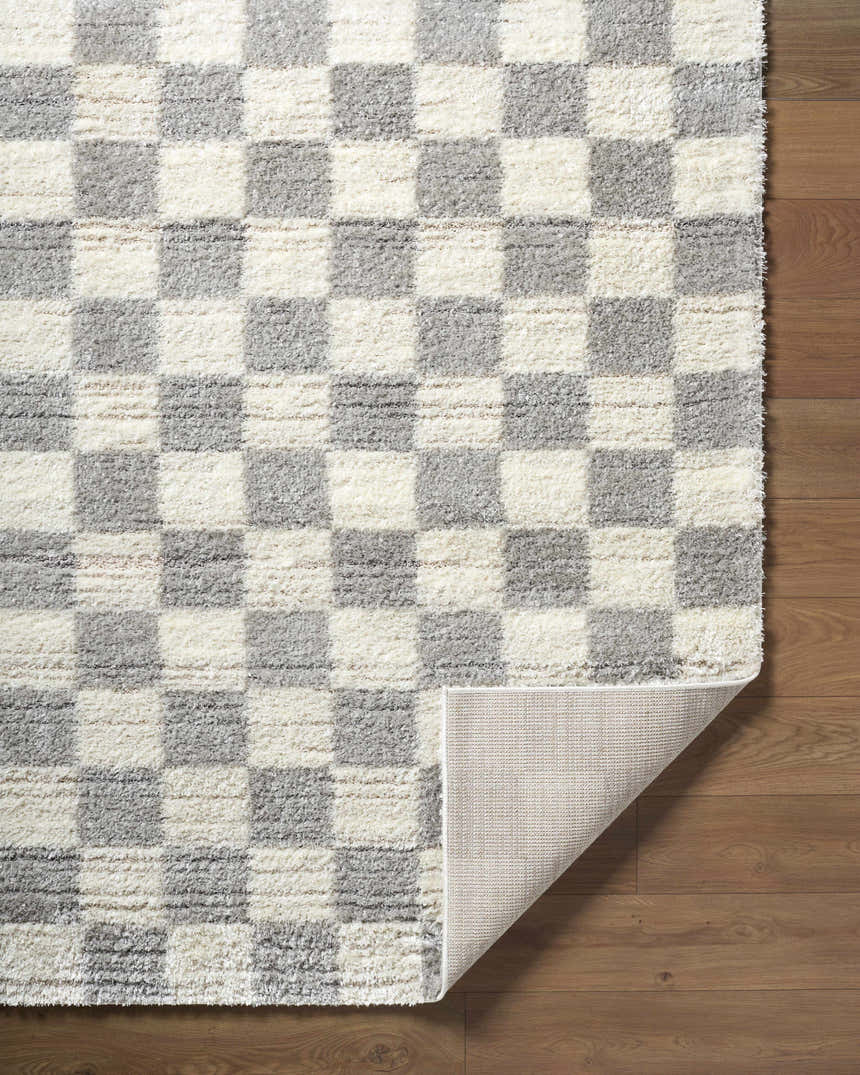 Close-up of Belita Tan Luxe Shag Area Rug with cream and light gray checkerboard pattern on a wood floor. Fold