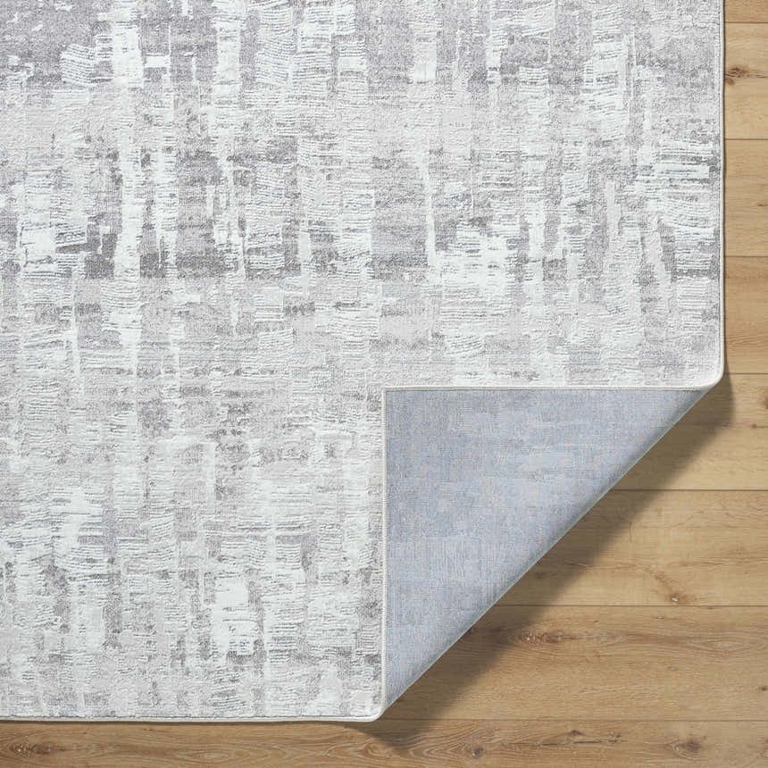 Close-up of the Branka Area Rug showing its light silver and gray contemporary pattern and texture on wood floor. Fold