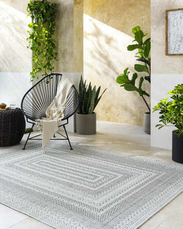 Sunlit living room scene with a gray and white Bernal Area Rug, chair, and plants. Roomscene-Rectangle