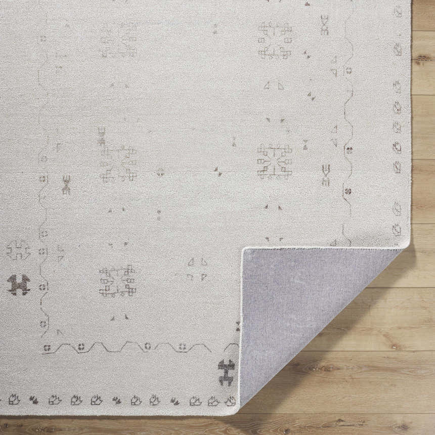 Close-up of the hand-tufted Bhavna Area Rug. Ivory rug with a subtle sandstone and taupe traditional pattern. Polyester rug on wood floor. Fold