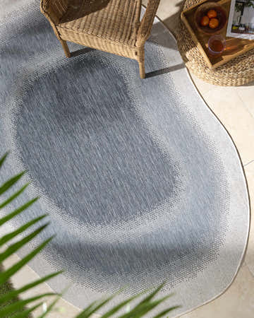 Outdoor patio scene with a blue and cream Burian Blue Area Rug, wicker chair, and side table. Roomscene-Custom