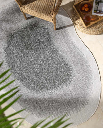 Outdoor patio scene with a Burian Charcoal Area Rug, wicker chair, and side table with drinks. Roomscene-Custom