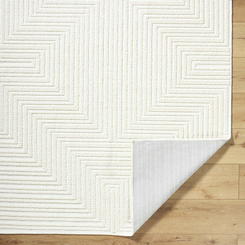 Close-up of Briana Off-White Washable Area Rug showing geometric design, plush texture, and non-slip backing on wood floor. Fold