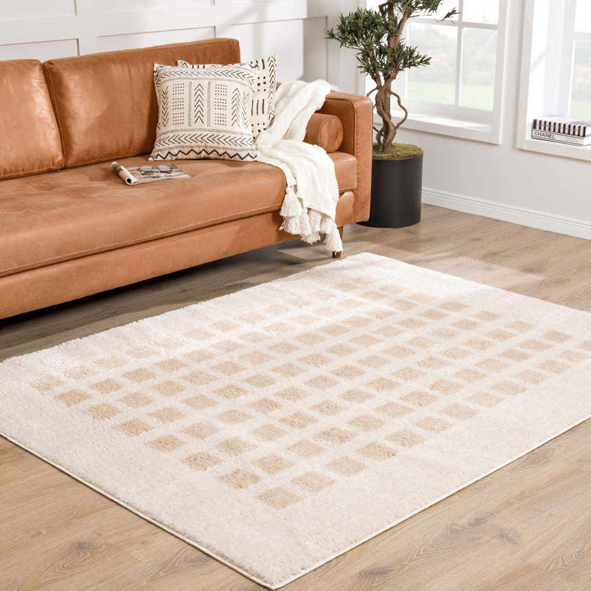 Living room scene with a Baback Beige Washable Area Rug, tan leather sofa, and light wood floors. Modern, neutral tones. Roomscene-Rectangle