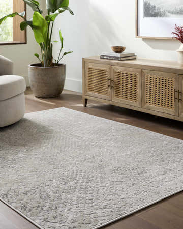 Living room scene with a cream armchair and light wood cabinet featuring the Basima Area Rug in cream, ivory, and light gray. Roomscene-Rectangle