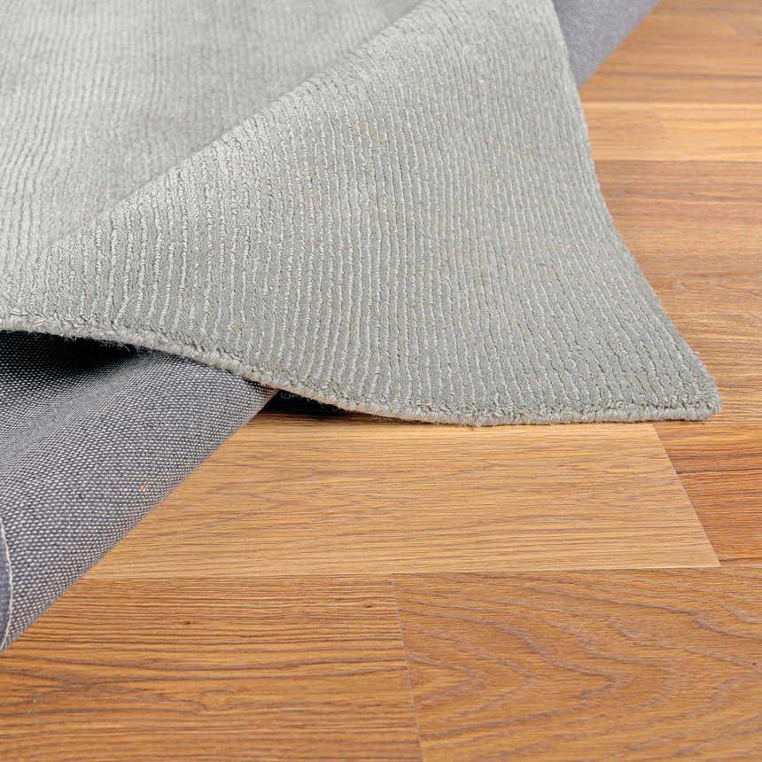 Close-up of the light gray Brockton Wool Rug showing its texture and backing on a wood floor. Fold