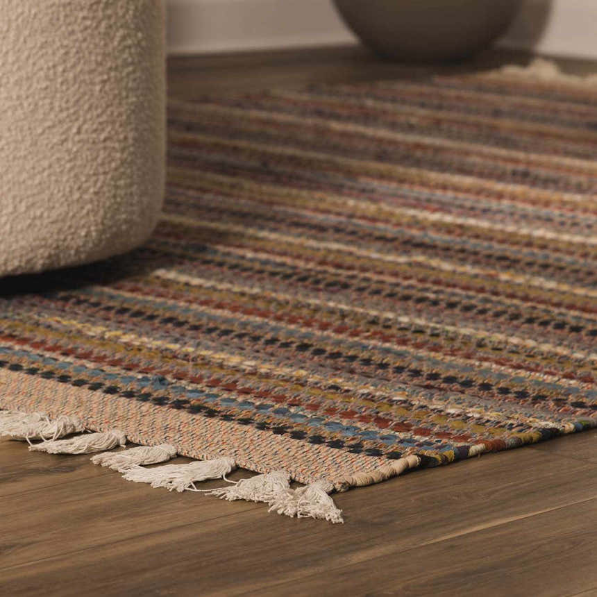 Close-up of the hand woven Brenda Crimson Area Rug with colorful stripes and tassels on a wood floor. Roomscene-Rectangle