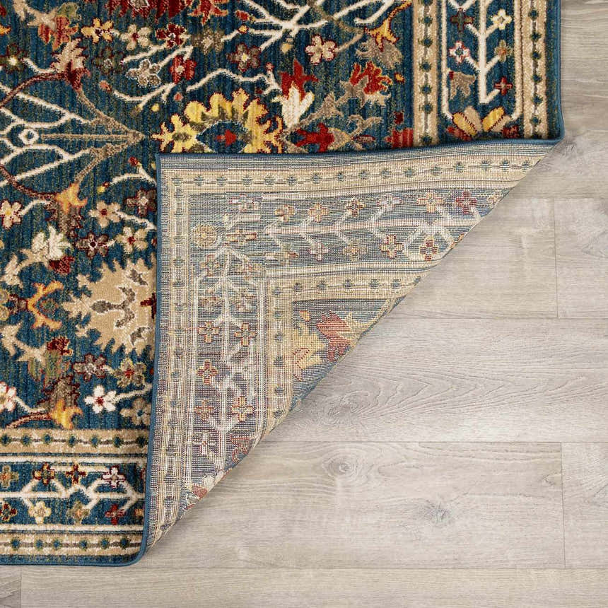 Close-up of the Neola Navy Blue Damask Area Rug showing its floral pattern, colors (navy, red, yellow, tan), and backing. Fold