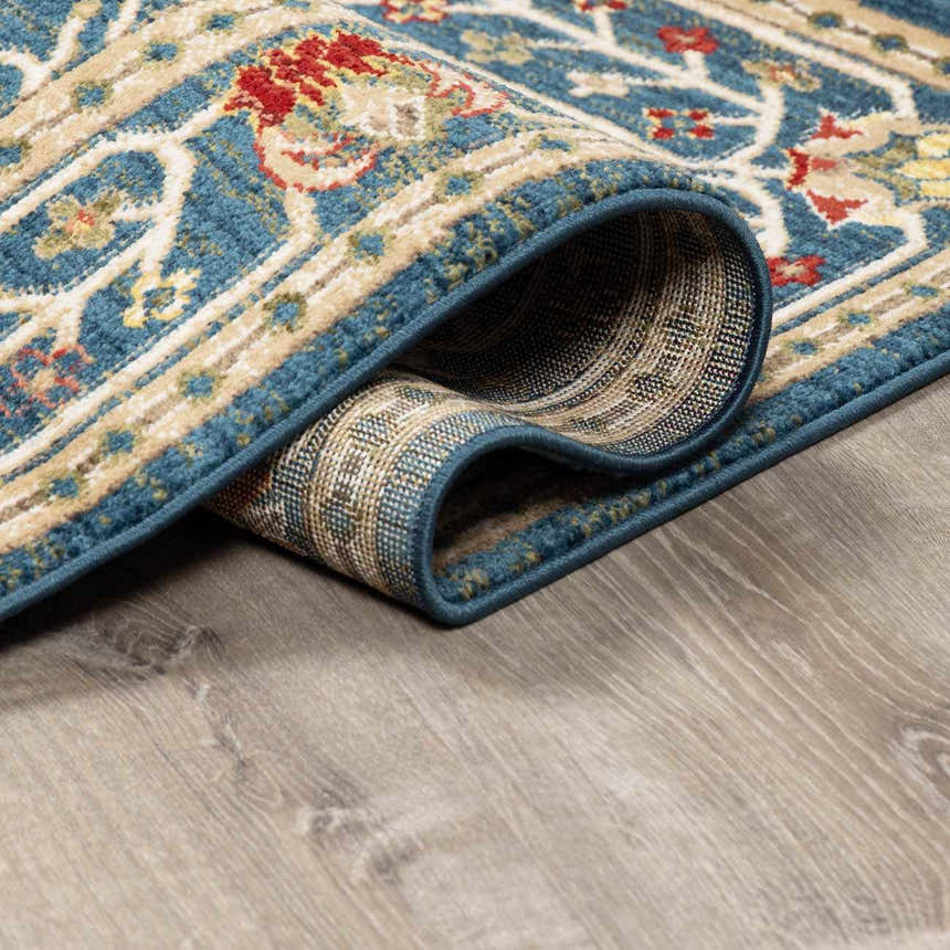 Close-up of the rolled edge of a Neola Navy Blue Damask Area Rug showing the traditional pattern and texture. Fold