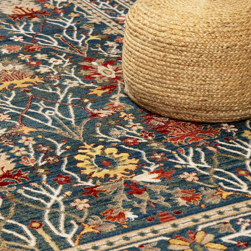 Close-up of the Neola Navy Blue Damask Area Rug showing its floral pattern, texture, and colors next to a jute pouf. Styleshot