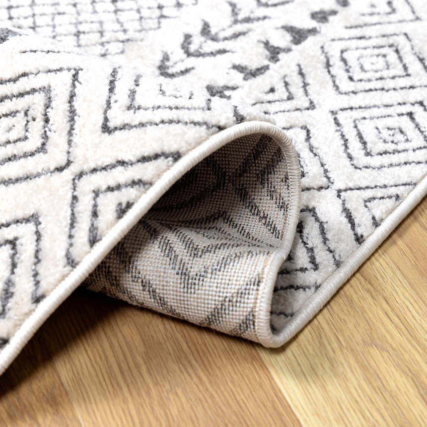 Close-up of the Burdette Soft Neutral Rug showing its geometric charcoal and beige pattern and soft texture. Fold