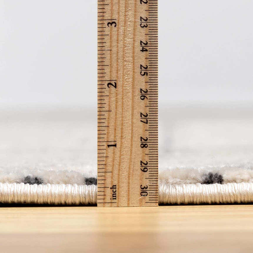 Close-up of Burdette Soft Neutral Rug pile height, showing charcoal and off-white fibers with a ruler for scale. Pile