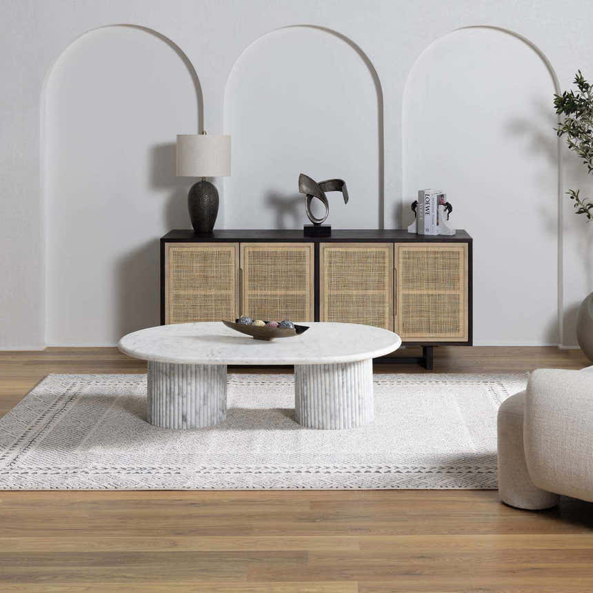 Living room scene with Burdette Soft Neutral Rug, marble coffee table, and cane cabinet against arched wall. Roomscene-Rectangle