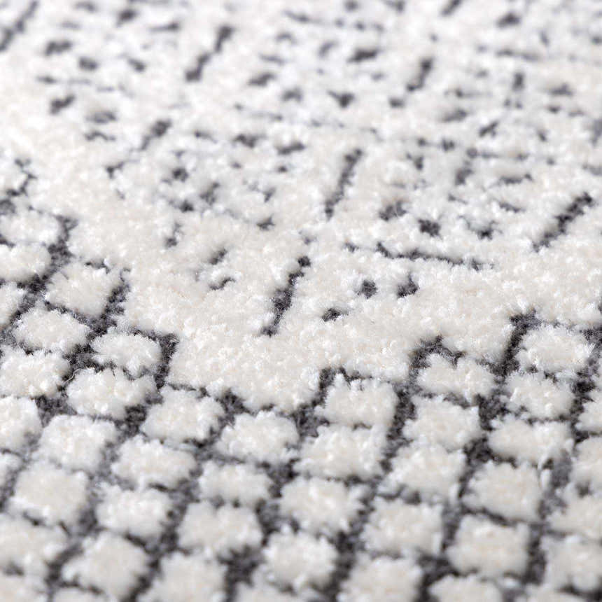 Close-up of the Burdette Soft Neutral Rug. Features a textured, off-white pattern on a charcoal gray base. Texture