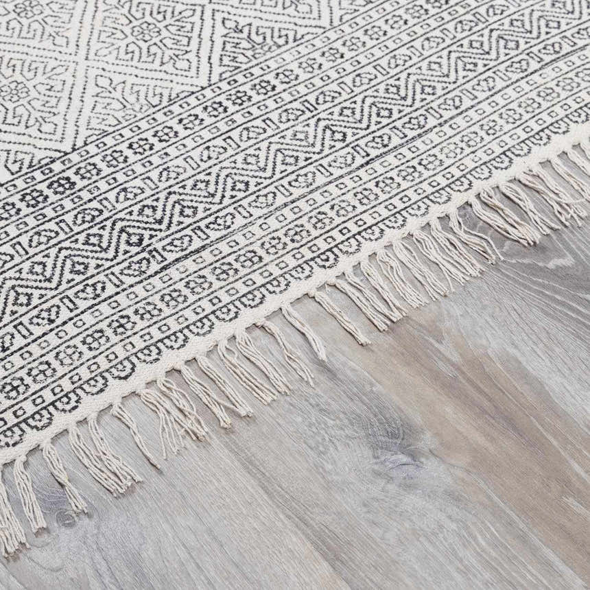 Close-up of the Brushton Area Rug. Beige cotton rug with black geometric pattern and fringe. Hand woven rug. Pile