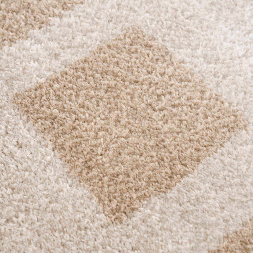 Close-up of the plush Beynon Beige Washable Area Rug, showing its beige and peach geometric design and soft texture. Texture