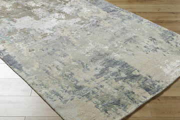 Close-up of the Bued Handmade Wool-Blend Rug. Abstract design in beige, brown, gray, and teal on a wood floor. Corner