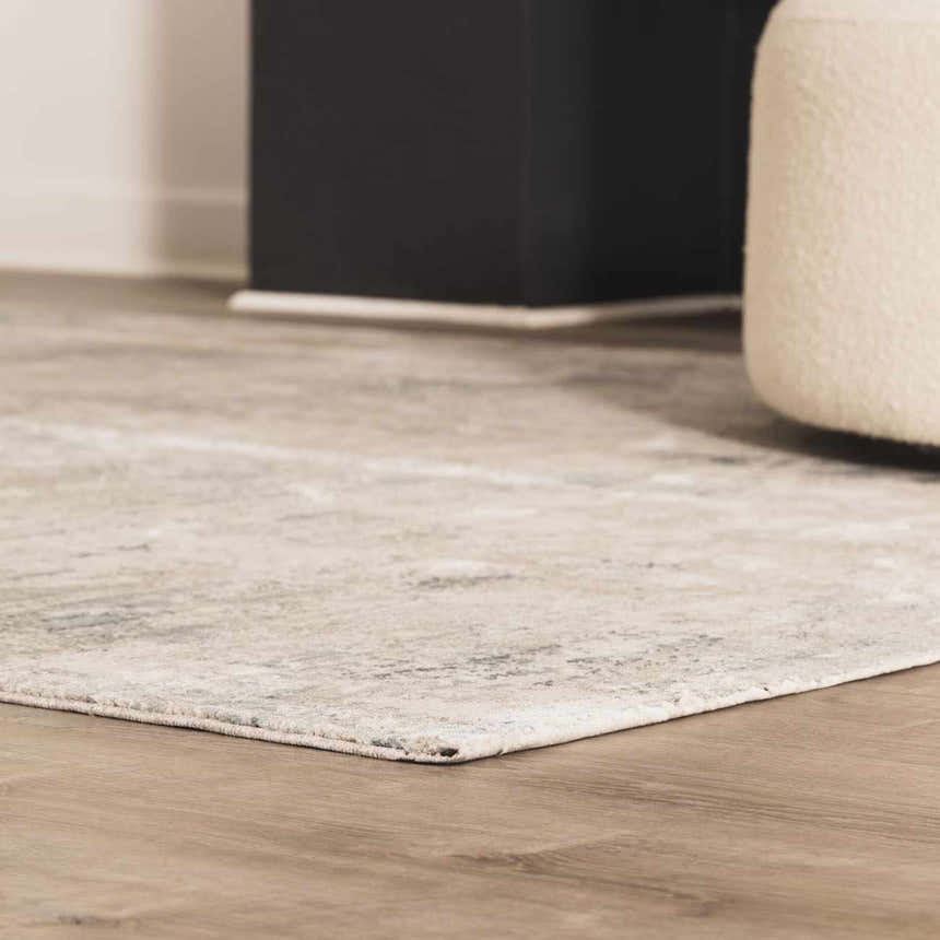Close up of the taupe and sage Burstwick Thick Luxe Boutique Rug on wood floor with a black cabinet and cream pouf. Styleshot