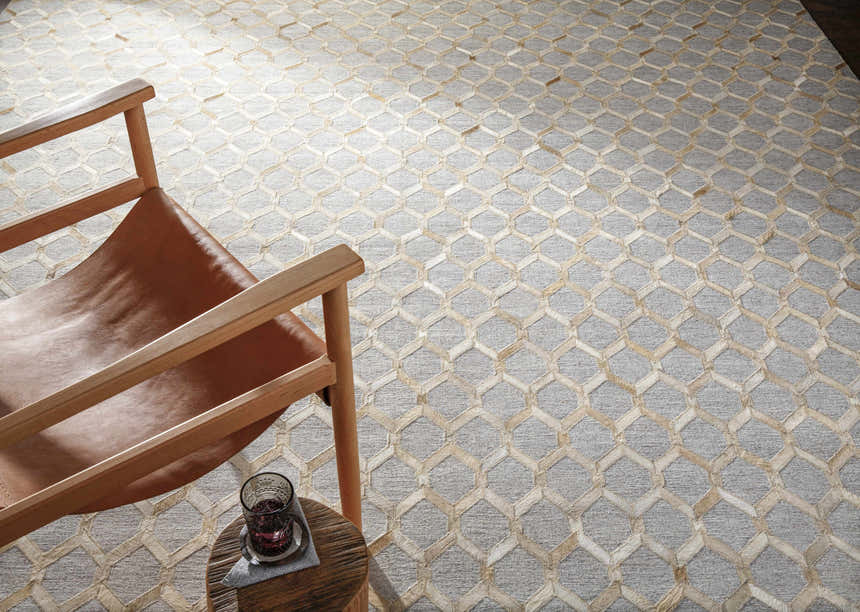 Living room scene with a tan leather chair on a Byng Premium Rug. The rug has a cream and gray geometric pattern. Styleshot