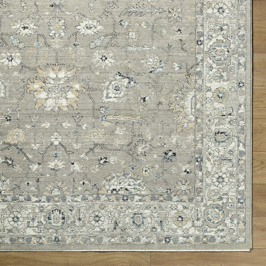 Close-up of a Briony Area Rug showing a traditional floral pattern in shades of gray, white, and blue on a wood floor. Corner