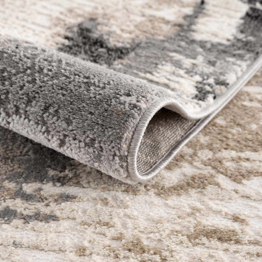 Close-up of the Birdie Area Rug showing its ash, light silver, and silver gray contemporary pattern and soft texture. Fold