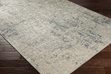 Close-up of Cayuga Area Rug in dark blue, sage, and off-white on dark wood floor. Contemporary silk rug texture. Corner