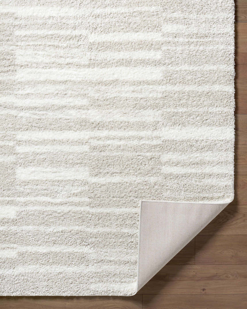 Close-up of the ivory Carlen Area Rug featuring a subtle horizontal stripe pattern and shag texture. Fold