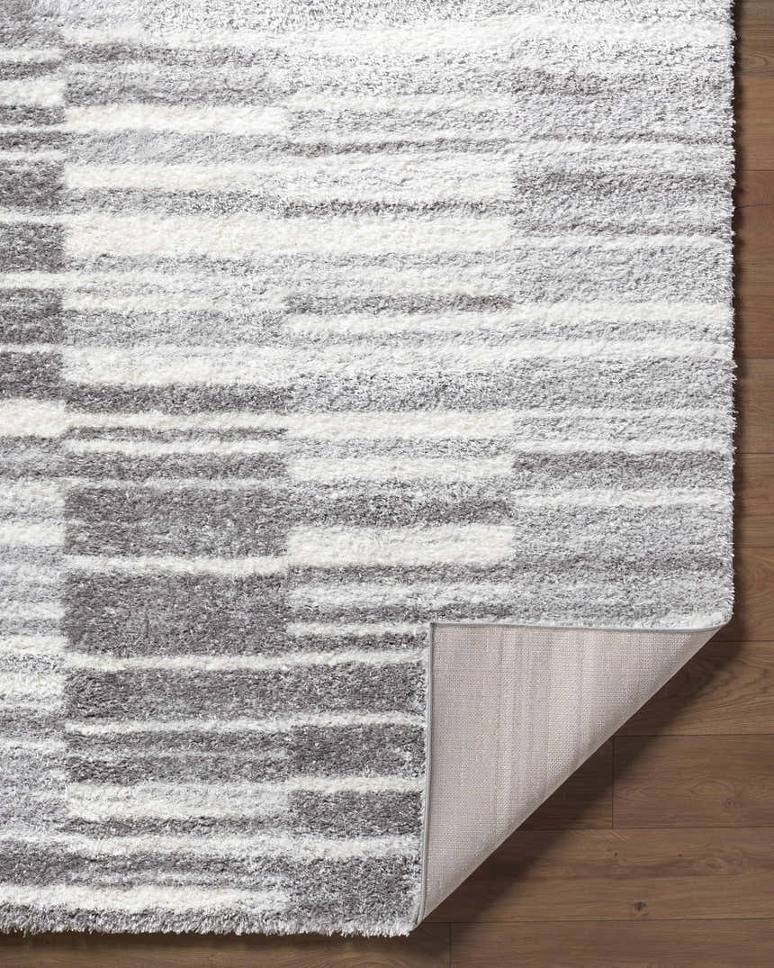 Close-up of the Carlen Gray Area Rug showing its gray and ivory shag texture and machine-woven construction. Fold