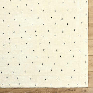 Close-up of the ivory Cirila Dotted Wool Rug showing the charcoal dots and soft, hand-tufted wool texture. Swatch