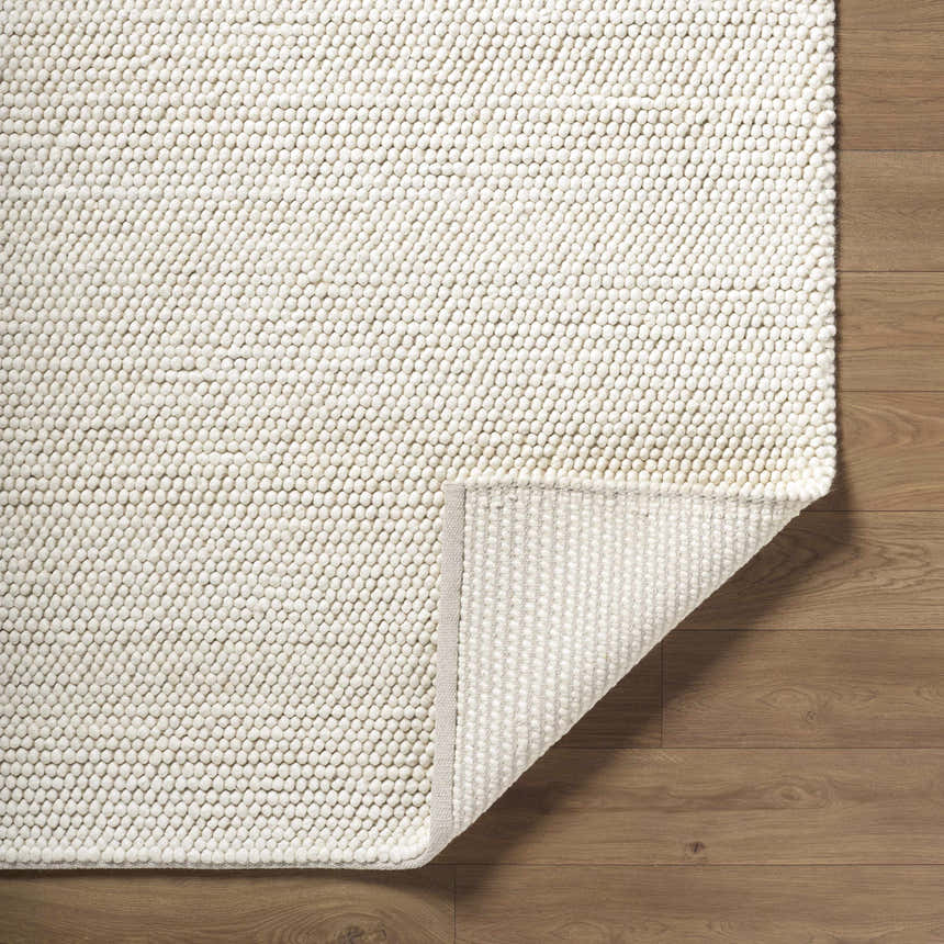 Close-up of the hand-woven Clayne Beige Premium Wool Area Rug showing its textured, looped design on a wood floor. Fold