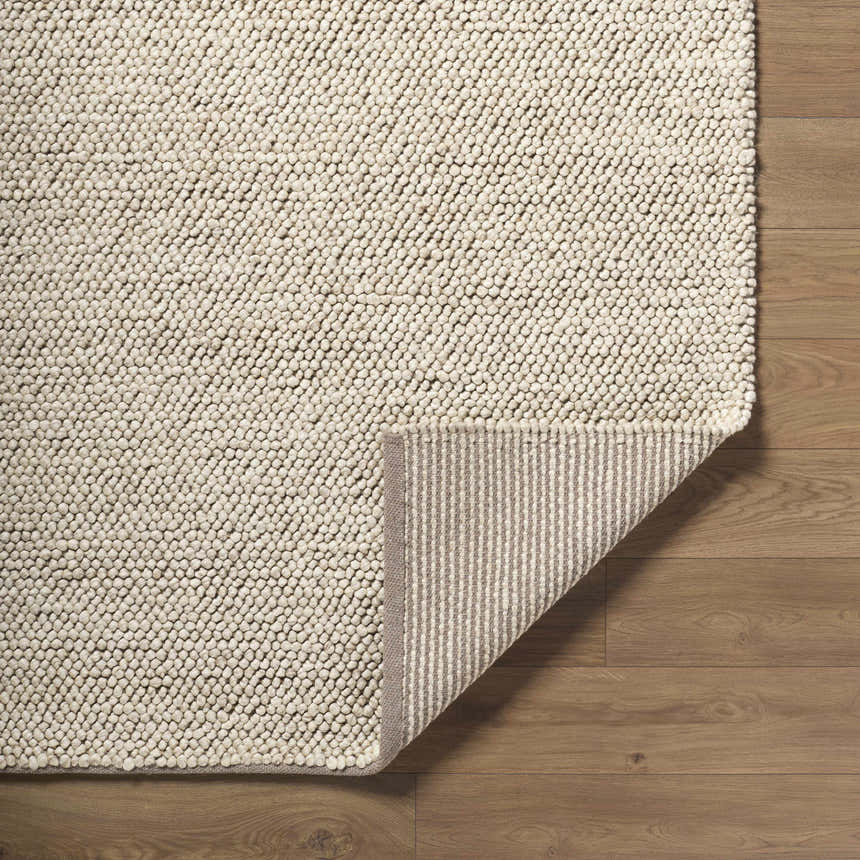 Close-up of the hand woven Clayne Dark Beige wool rug showing the looped texture and striped backing on wood floors. Fold